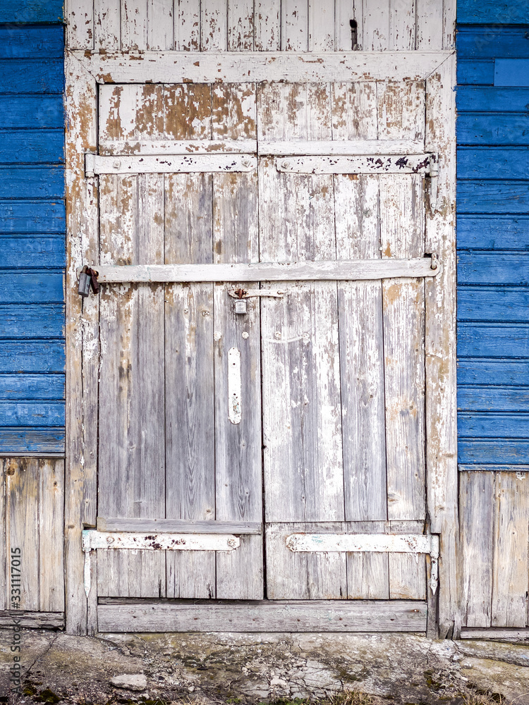 weathered white painted closed door with cracked and flaked paint. blue wooden wall background weathered white painted closed door with cracked and flaked paint. blue wooden wall background