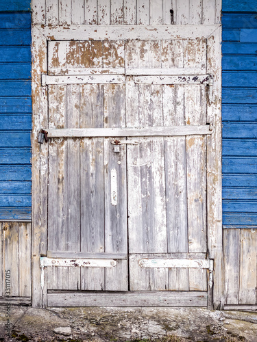 weathered white painted closed door with cracked and flaked paint. blue wooden wall background