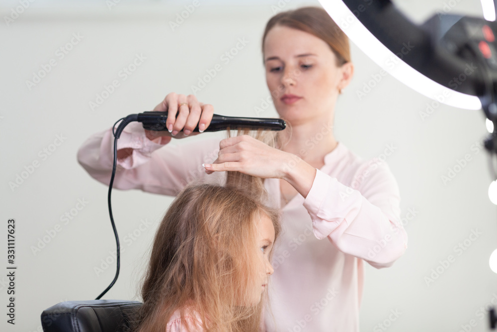 The work of the stylist on hairstyles in a bright salon, the girl makes curls and braids braids of a small beautiful model, The work of the stylist on hairstyles in a bright salon, the girl makes curls and braids braids of a small beautiful model,
