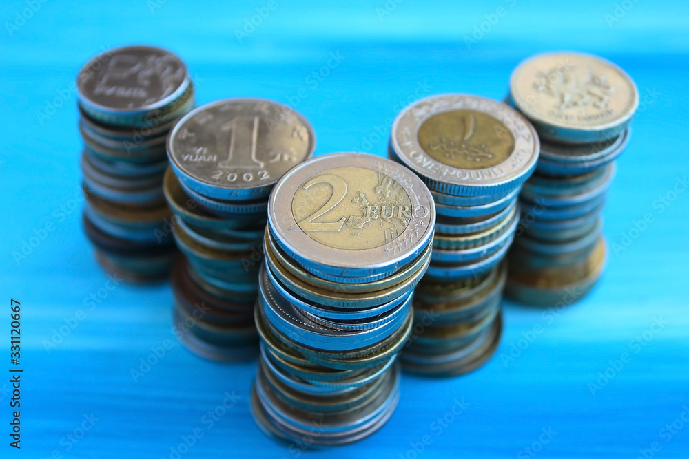 Stacks of coins in a row of different countries, on a blue background. Coins two euros, one yuan, one pound Stacks of coins in a row of different countries, on a blue background. Coins two euros, one yuan, one pound