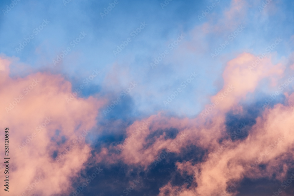 Close up of a layer of clouds colored in sunset colors moving across a bright blue sky