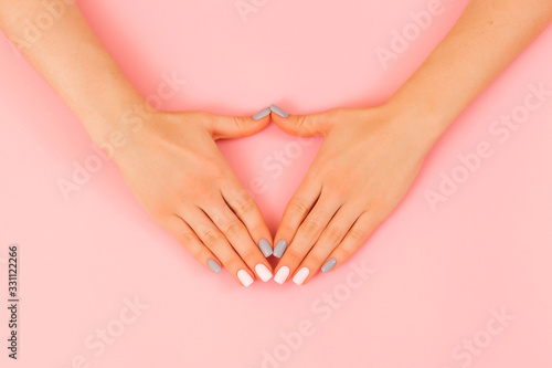 Hands of a beautiful woman on a pink background. Delicate hands with natural manicure, clean skin. Light pink gray nails. © Konstantin