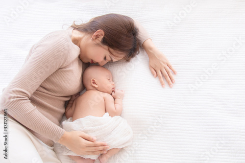 Asian beautiful mom motherhood lie down nursing, kissing newborn baby infant toddler, gently hold together on chest with love, infant sleep comfortable with safe and protection by mother taking care photo