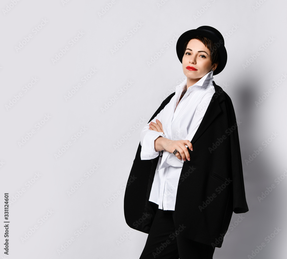 Young woman in stylish hat, black jacket and shirt is posing with her arms crossed over white background with copy space Young woman in stylish hat, black jacket and shirt is posing with her arms crossed over white background with copy space