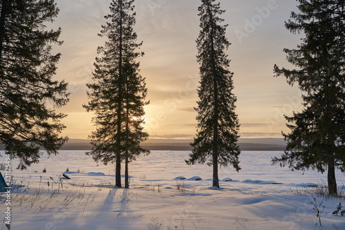  Snow- covered lake at dawn with boats on the shore. Winter forest with snow-covered fir trees high in the mountains. Sunny February day in the spruce forest. 
