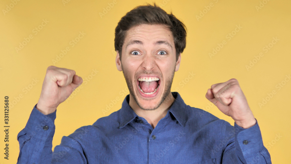 Casual Young Man Celebrating Success on Yellow Background Casual Young Man Celebrating Success on Yellow Background
