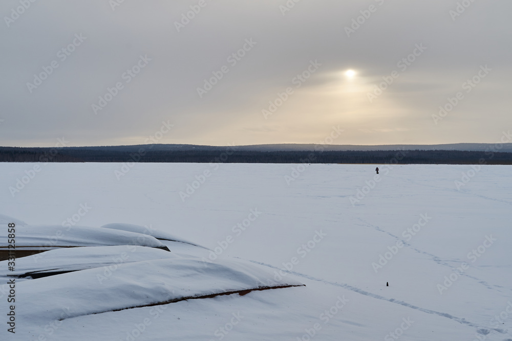 Snow- covered lake at dawn with boats on the shore. Winter forest with snow-covered fir trees high in the mountains. Sunny February day in the spruce forest. Snow- covered lake at dawn with boats on the shore. Winter forest with snow-covered fir trees high in the mountains. Sunny February day in the spruce forest.