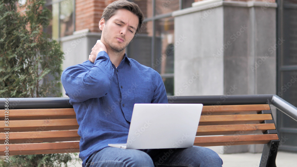 Sitting Outdoor, Young Man with Neck Pain working on Laptop Sitting Outdoor, Young Man with Neck Pain working on Laptop