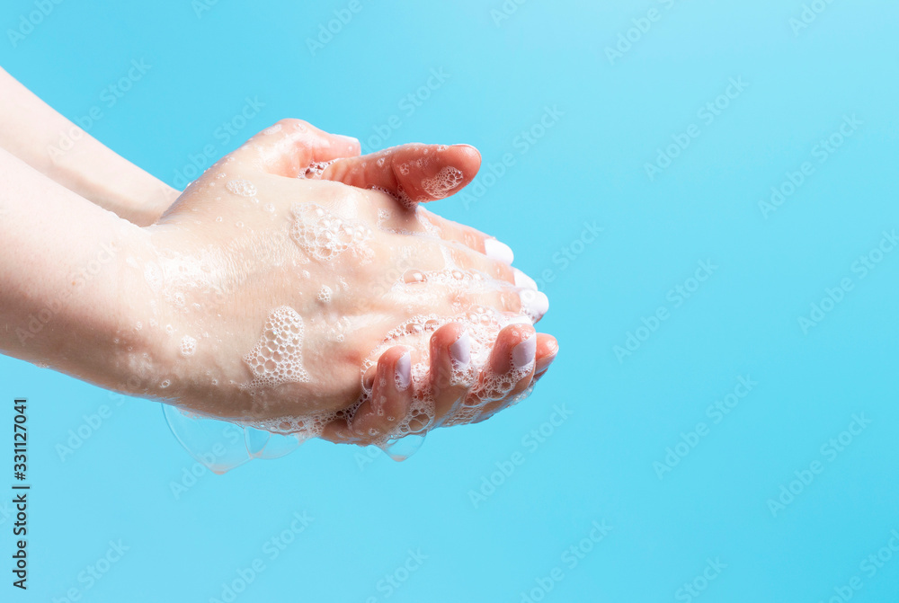 Fototapeta premium Girl washes her hands with soap close up on a blue background.