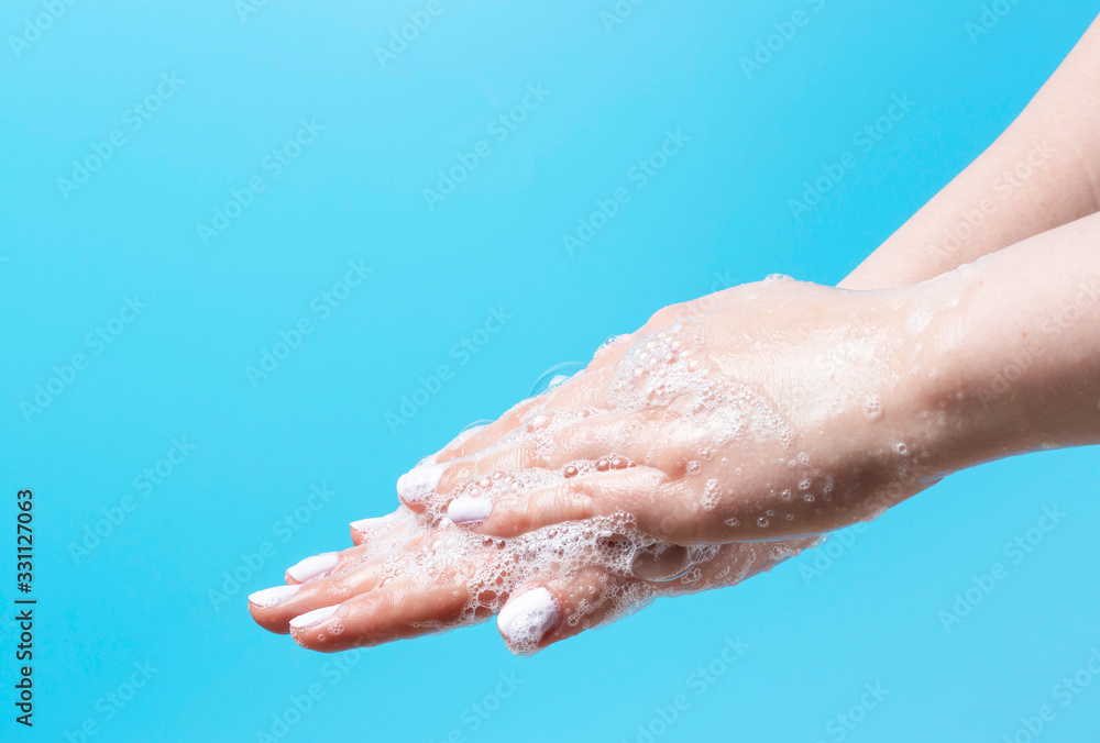 Fototapeta premium Girl carefully washes her hands with soap close-up on blue background, copy space