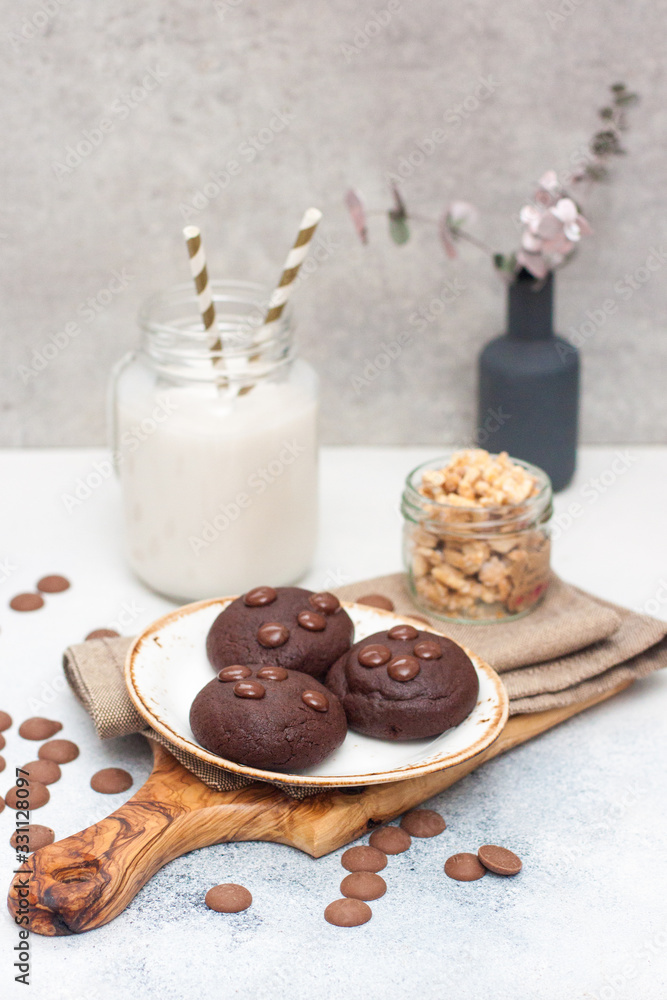 Chocolate cookies with choco drops on white plate, and glass of milk Chocolate cookies with choco drops on white plate, and glass of milk