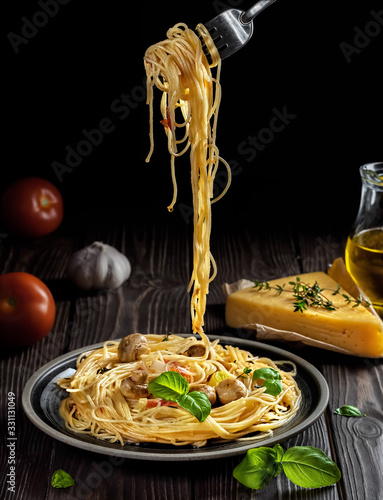 The plate of pasta with cheese, mushrooms and vegetables, on a dark wooden background. Spaghetti fork raised above the dish. Close-up, shallow depth of field. The concept of a vegetarian lunch.