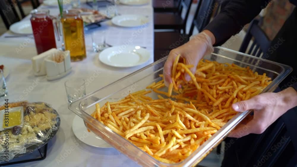 waiter wearing gloves puts plate of fries. waiter wearing gloves puts plate of fries.