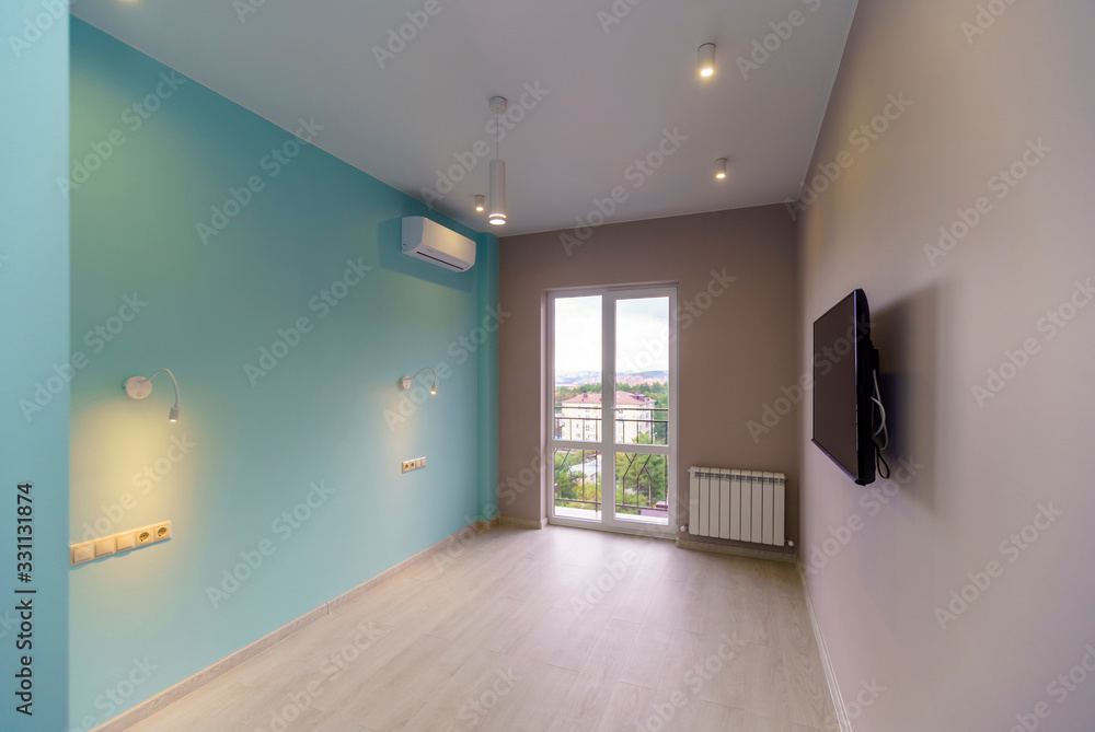 An empty room with green walls, a TV and a window in a new apartment with a fresh renovation. On the floor laminate An empty room with green walls, a TV and a window in a new apartment with a fresh renovation. On the floor laminate