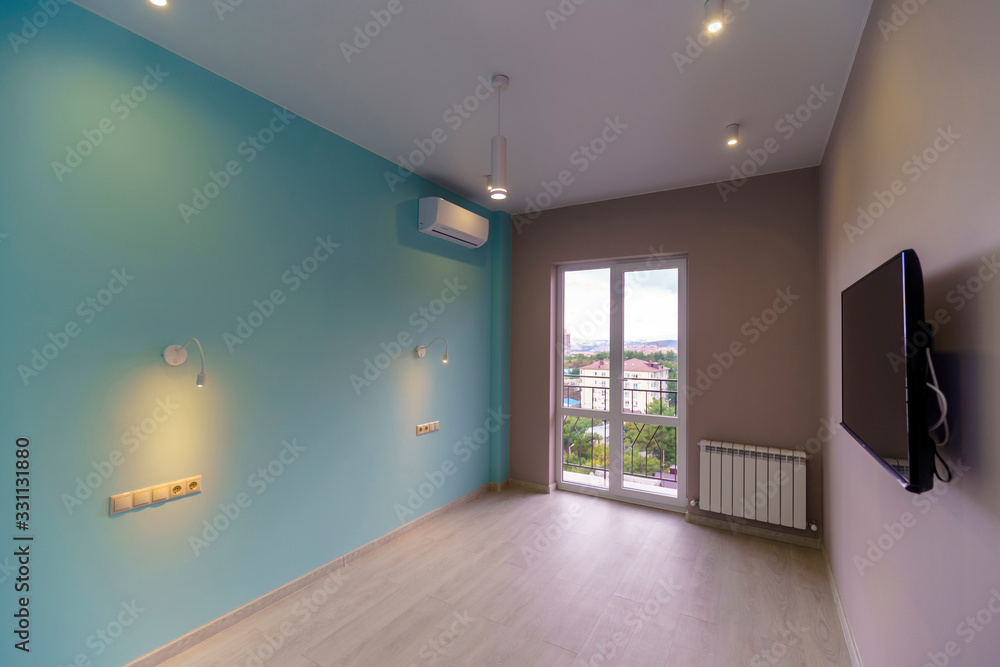 An empty room with green walls, a TV and a window in a new apartment with a fresh renovation. On the floor laminate An empty room with green walls, a TV and a window in a new apartment with a fresh renovation. On the floor laminate