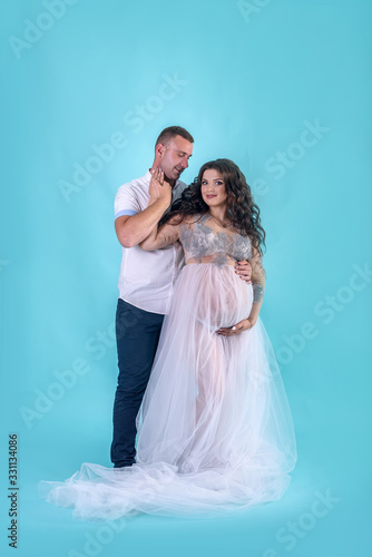 Happy pregnant couple. Handsome husband hugging his beautiful wife in studio