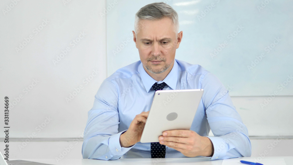 Senior Businessman Browsing Internet on Tablet in Office Senior Businessman Browsing Internet on Tablet in Office