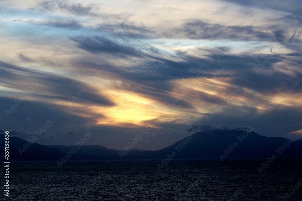 evocative image of sunset over the sea with headland silhouette in the background evocative image of sunset over the sea with headland silhouette in the background