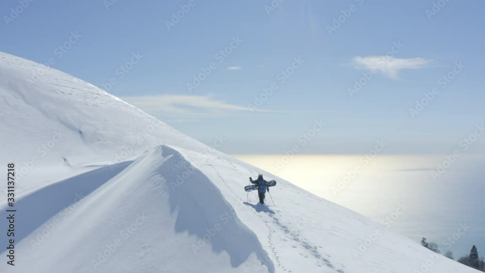 Snowboarder track climbing on snowy peak winter mountain with sea landscape. Drone aerial view man with snowboard walking to snowy peak with sticks for ride. Winter hiking for freeride extreme sport Snowboarder track climbing on snowy peak winter mountain with sea landscape. Drone aerial view man with snowboard walking to snowy peak with sticks for ride. Winter hiking for freeride extreme sport
