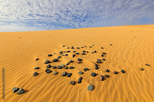 Summer dry landscape in Africa. Black pebble stones. Sandy waves in the wild nature. Dunas Maspalomas, Gran Canaria, Spain. Beautiful rare blue sky with white clouds.