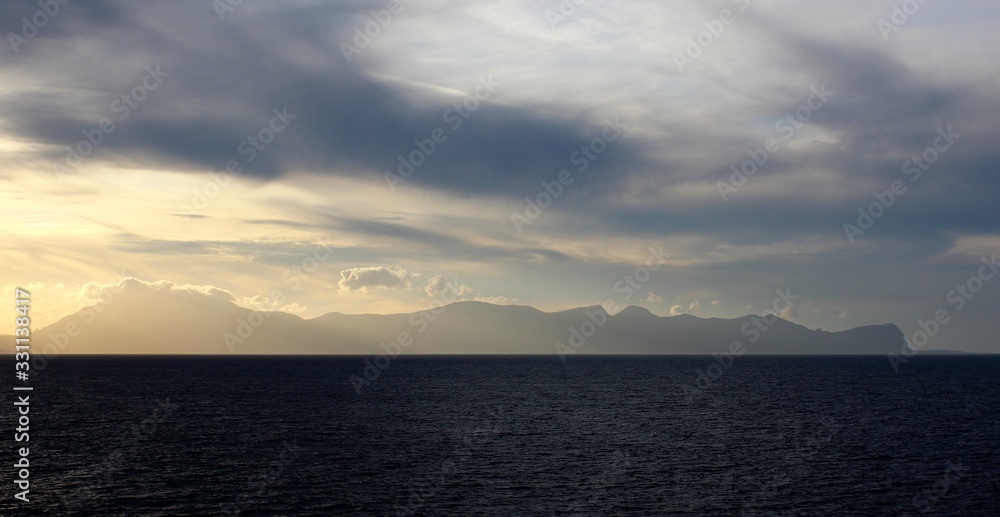 evocative image of sunset over the sea with headland silhouette in the background evocative image of sunset over the sea with headland silhouette in the background