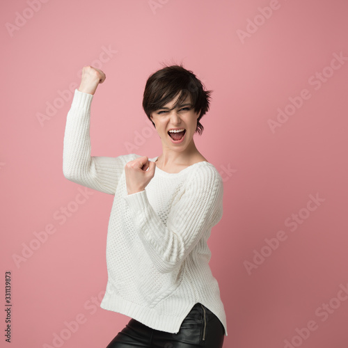 Beautiful young woman happy and excited expressing winning gesture. Successful and celebrating victory, triumphant, studio shot over pink background photo