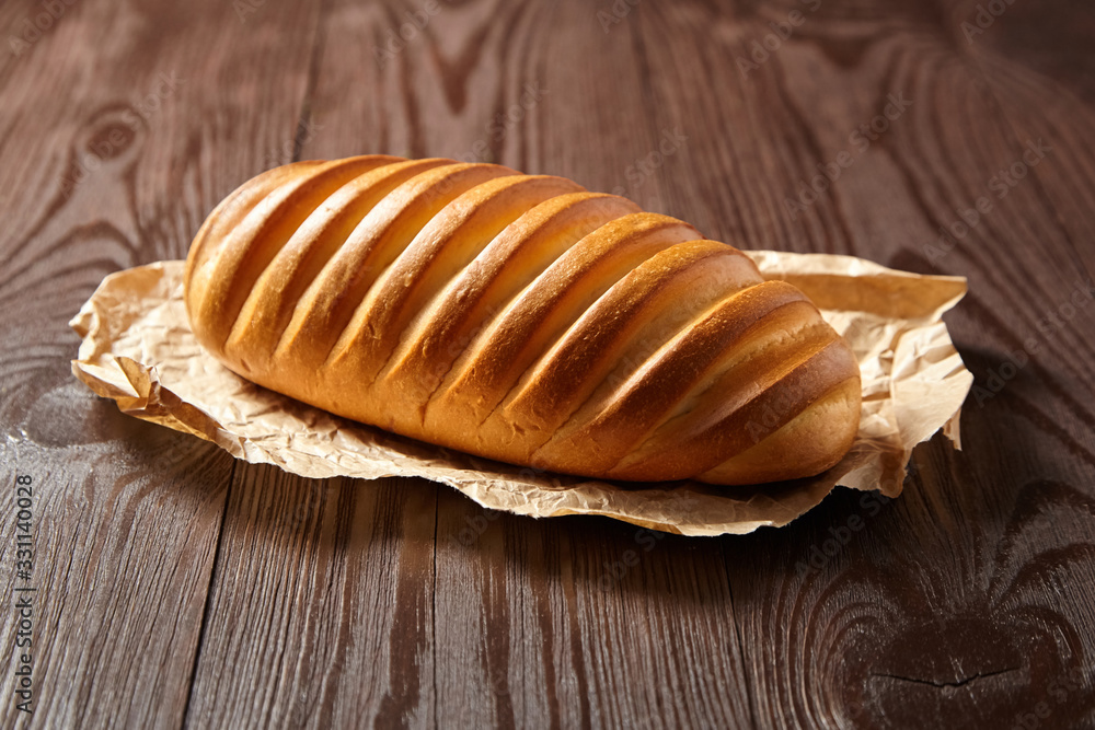 Bakery product. Baked whole bun on wooden table. Loaf, white wheat bread on baking paper on brown background Bakery product. Baked whole bun on wooden table. Loaf, white wheat bread on baking paper on brown background