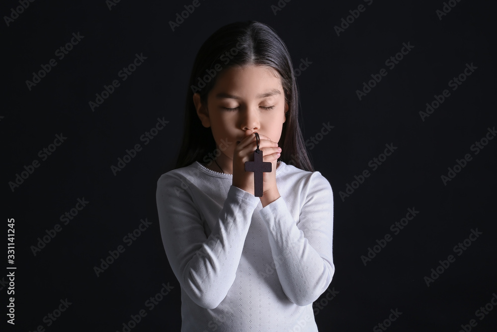 Cute little Asian girl praying on dark background Cute little Asian girl praying on dark background