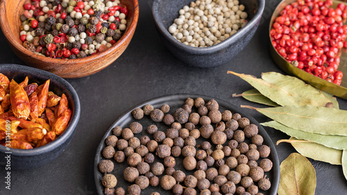 Different  spices , pepper type, black ,white, pink ,green, cayenne, allspice peppercorns and bay leaf in bowls on dark background.