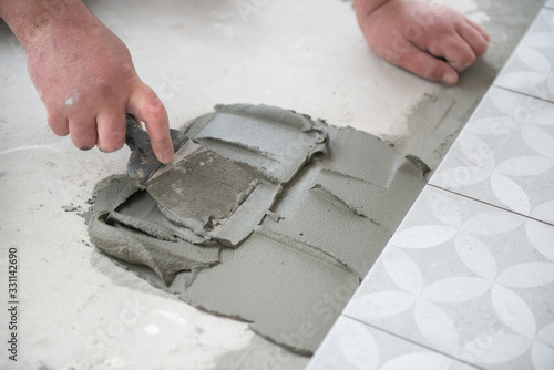 Tiler laying the ceramic tile on the floor. Professional worker makes renovation. Construction. Hands of the tiler. Home renovation and building new house