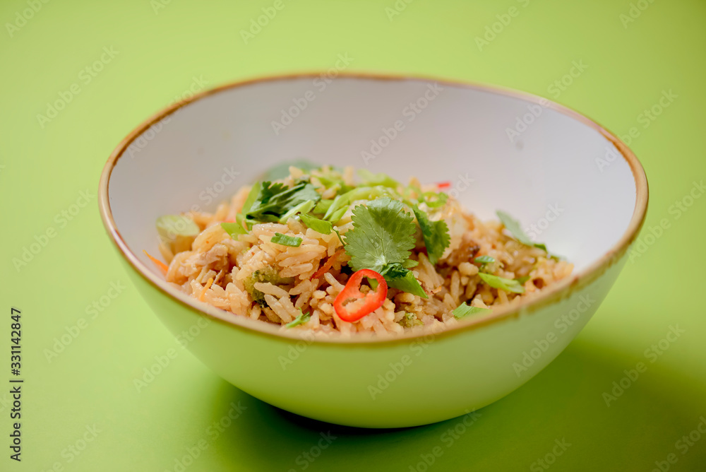 Japanese food rice served with vegetables in a white bowl over bright green background. Japanese cuisine isolated. Japanese food rice served with vegetables in a white bowl over bright green background. Japanese cuisine isolated.