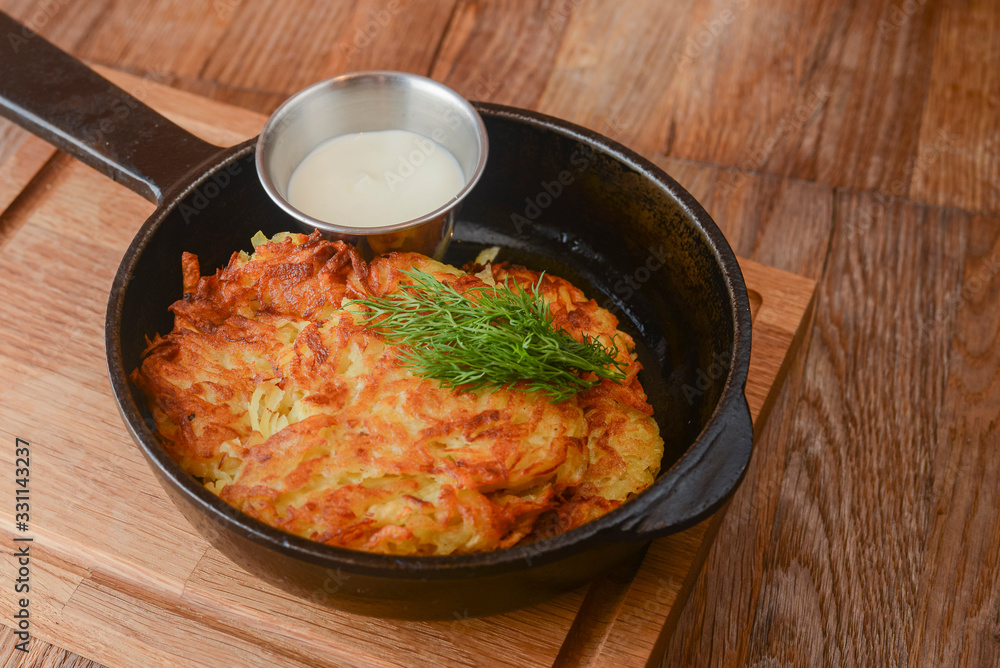 Delicious potato pancakes with cheese and herbs in a pan over light rustic wooden board. Dinner in restaurant. Delicious potato pancakes with cheese and herbs in a pan over light rustic wooden board. Dinner in restaurant.