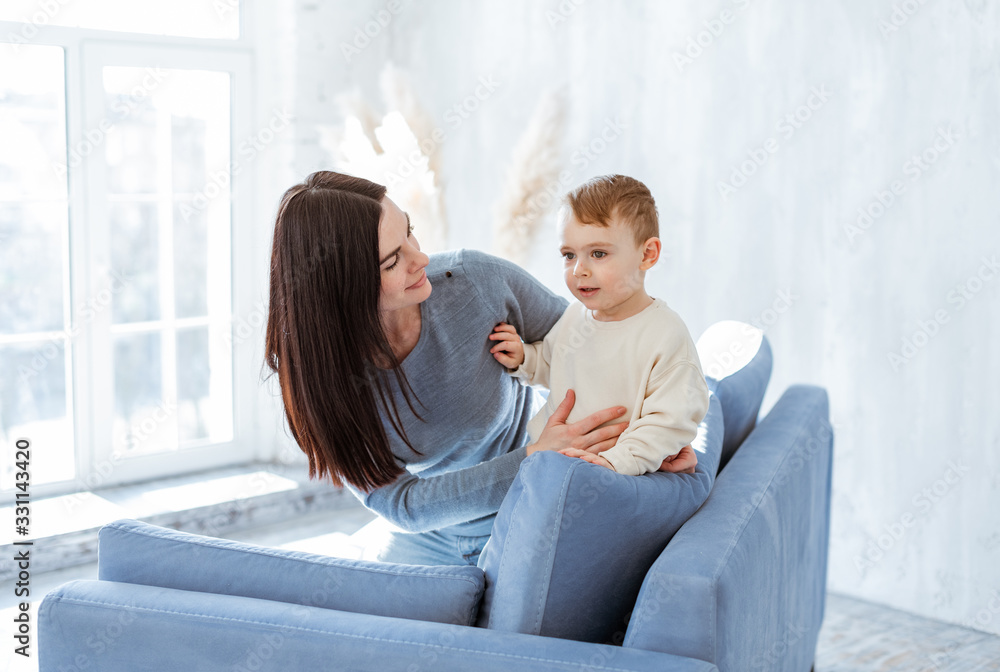 Mom hugs her little son sitting on a blue sofa in front of a large window.  Family time Stock-foto | Adobe Stock
