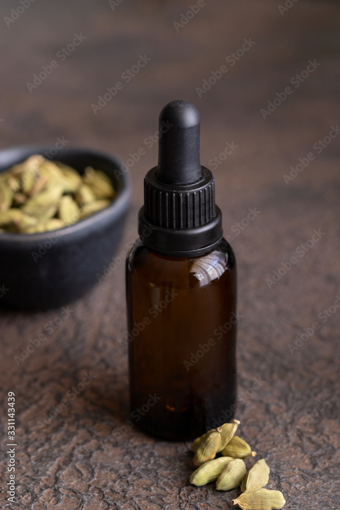 A dropper bottle of cardamomn essential oil and cardamom seeds on cocrete background. A dropper bottle of cardamomn essential oil and cardamom seeds on cocrete background.