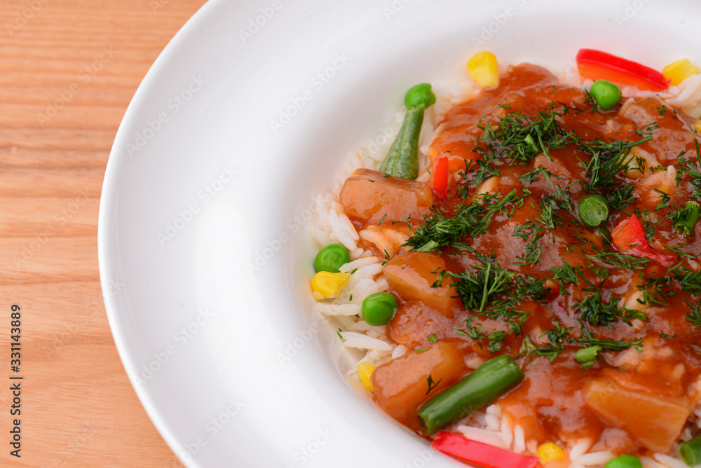 Rice with beef stew with green beans and vegetables served in white plate over light rustic wooden table. Rice with beef stew with green beans and vegetables served in white plate over light rustic wooden table.