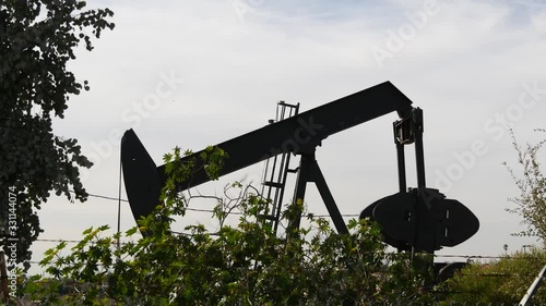 Industrial urban landscape. La Brea Inglewood in Los Angeles. Well pump jack operating behind the fence. Drilling rig extract crude oil. Oil mining machine with working piston. Oil and gas industry.