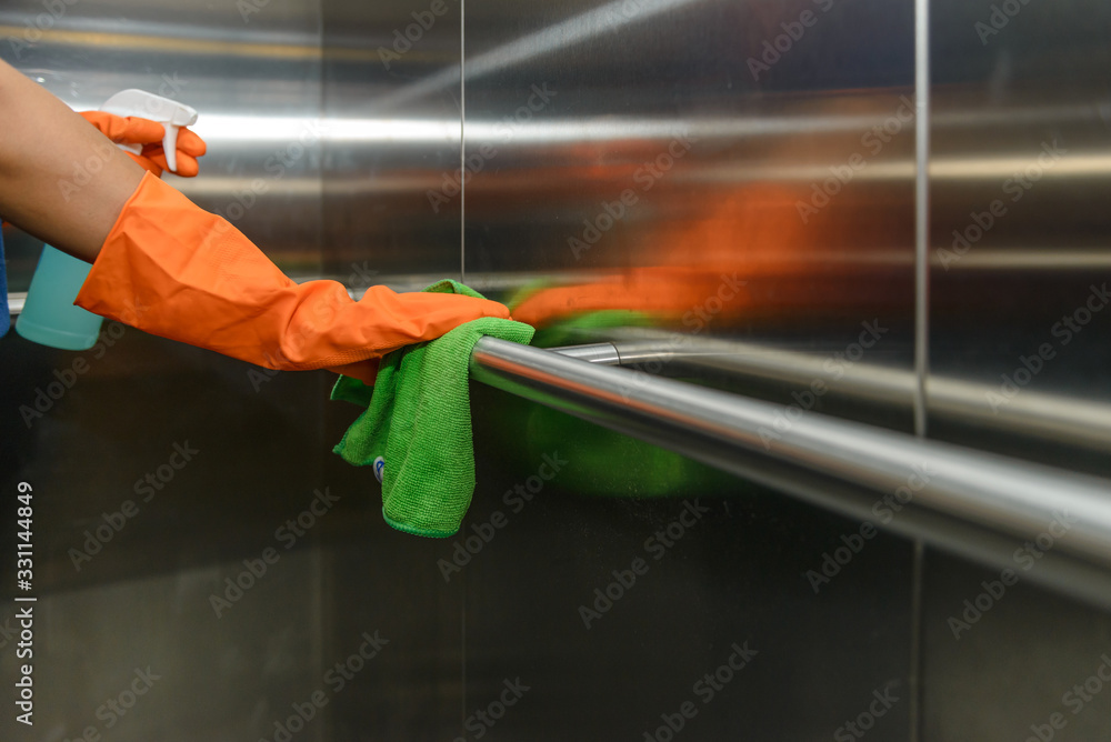 Woman hand in protective orange rubber gloves holding green microfiber cleaning cloth and wiping dust using a spray sterilizing solution make cleaning and disinfection for good hygiene - obrazy, fototapety, plakaty 