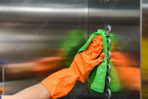 Woman hand in protective orange rubber gloves holding green microfiber cleaning cloth and wiping dust using a spray sterilizing solution make cleaning and disinfection for good hygiene photo