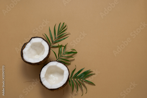 top view halves of coconut and green tropical leaves on a brown background copy space