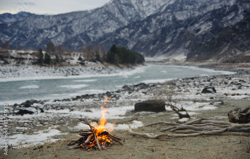 Camp piknic fire on the sand shore of mountain winter river under snow and ice