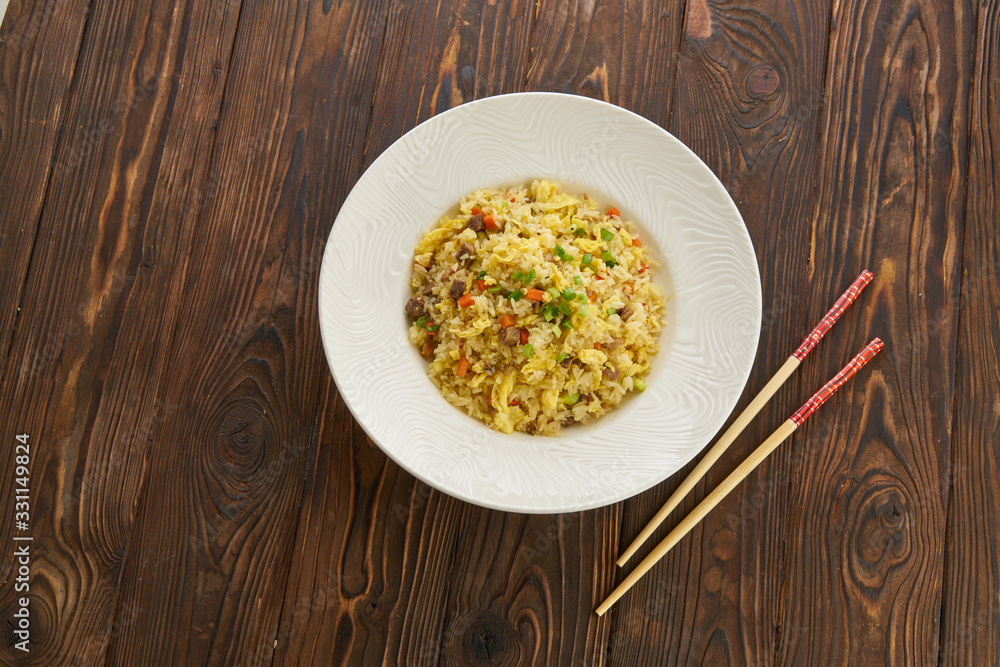 Fried rice with vegetables and beef in white plate, chopsticks on wooden background, Asian food concept, top view copy space Fried rice with vegetables and beef in white plate, chopsticks on wooden background, Asian food concept, top view copy space