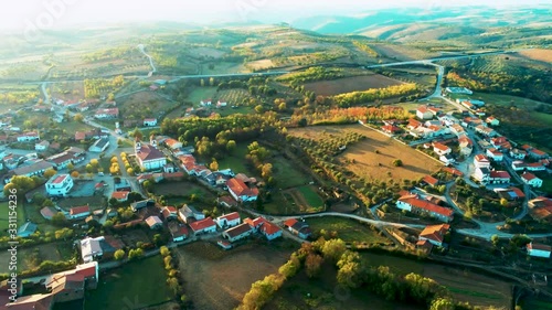 Slow aerial pan left of the Portuguese town of Outeiro, Portugal, sunset lens flare, rolling hills, vineyards, traditional white houses with red slate roofs photo
