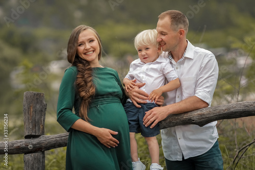A family of three stands near a wooden fence in the village.