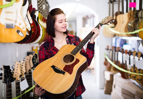 Charming teen girl examining various acoustic guitars