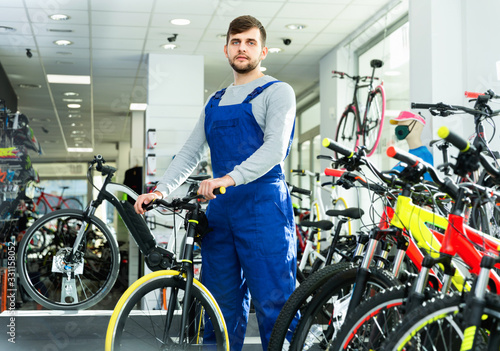 Portrait of young repairman standing near cycle in bicycle store