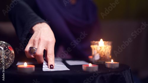 Fortuneteller female divines on cards sitting at table with burning candles, magic ball