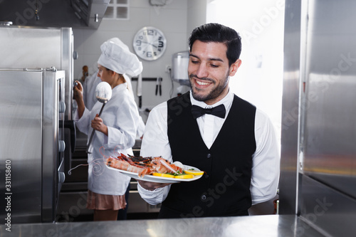 Waiter holding seafood dish in kitchen of restaurant