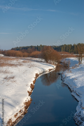 Winter landscape. A small river between two snow-covered banks against the background of forest and blue sky. Russian nature, Russian hinterland, province. © pattern43
