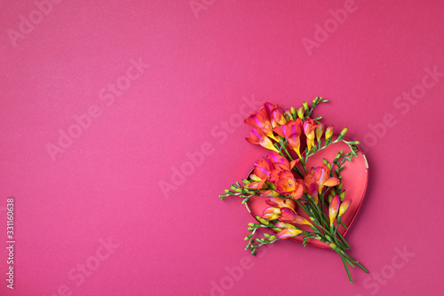 Spring freesia flowers over red heart on pink background. Top view. Flat lay. Summer and spring concept. Valentines day, Woman day concept. Spring or summer banner with copy space