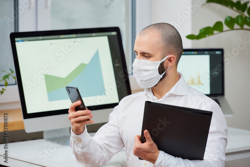 A manager wearing a protective mask against a virus. Doctor with a surgical mask against the 2019-nCoV using the phone and the other hand holding a folder in his office. Coronavirus quarantine.